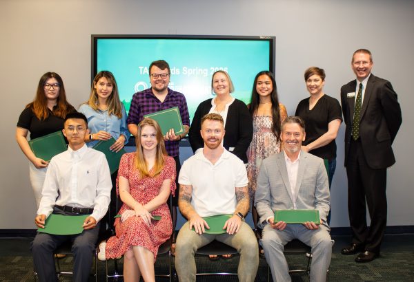 Graduate student award finalists sit in two rows with the dean to the right in front of a TV screen